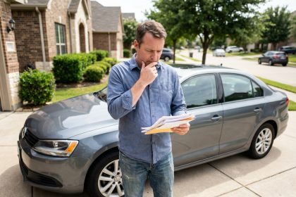 Homme d'&acirc;ge moyen v&eacute;rifiant ses papiers de voiture devant sa berline grise