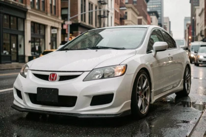 Honda Civic EP3 Type R blanche garée dans une rue urbaine mouillée, vue 3/4 avant sur fond de bâtiments flous