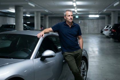 Homme passionné de Porsche appuyé contre sa 911 argentée dans un garage béton, réfléchissant à son assurance auto